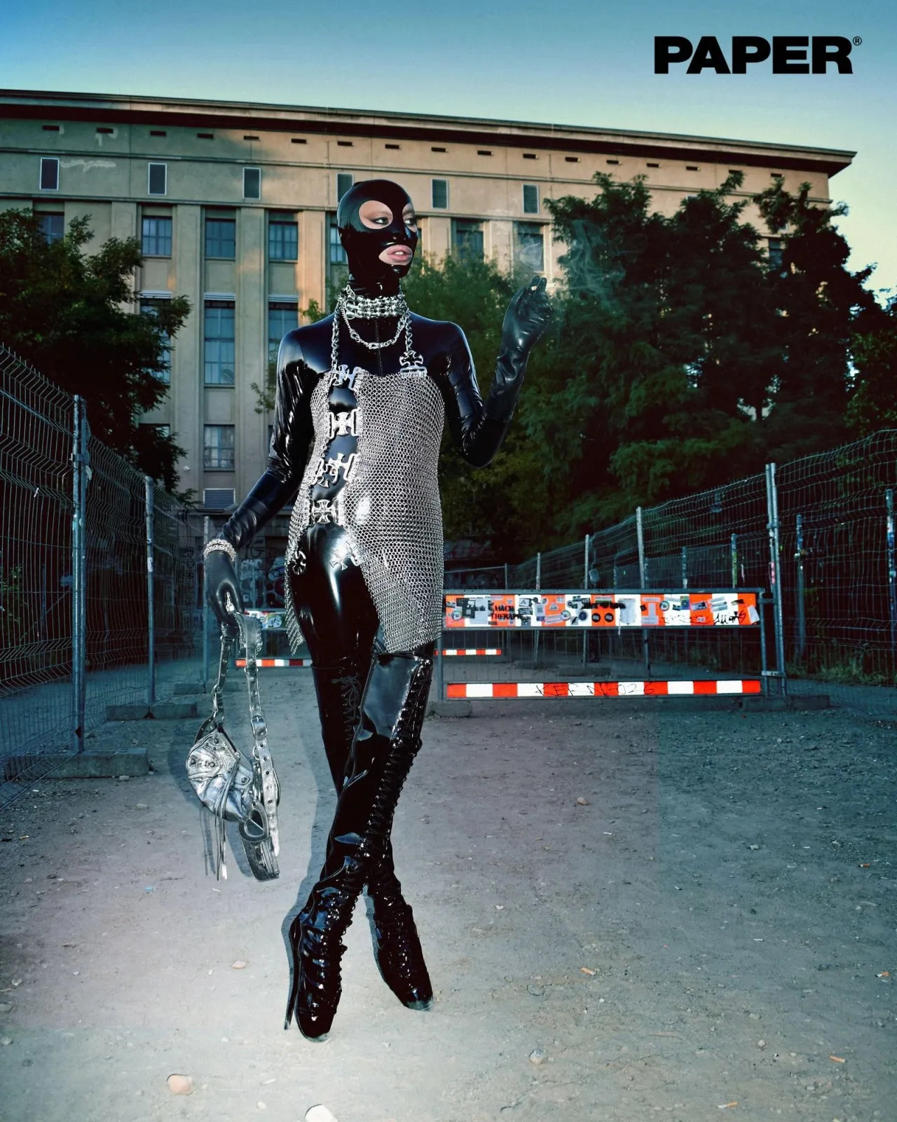 Berlin Techno Fashion aesthetic — This image perfectly captures the aesthetic with latex, harnesses, mesh, thigh-high boots, and a chainmail top, all set against a backdrop that evokes the industrial feel of Berlin clubs, with the iconic Berghain building visible.