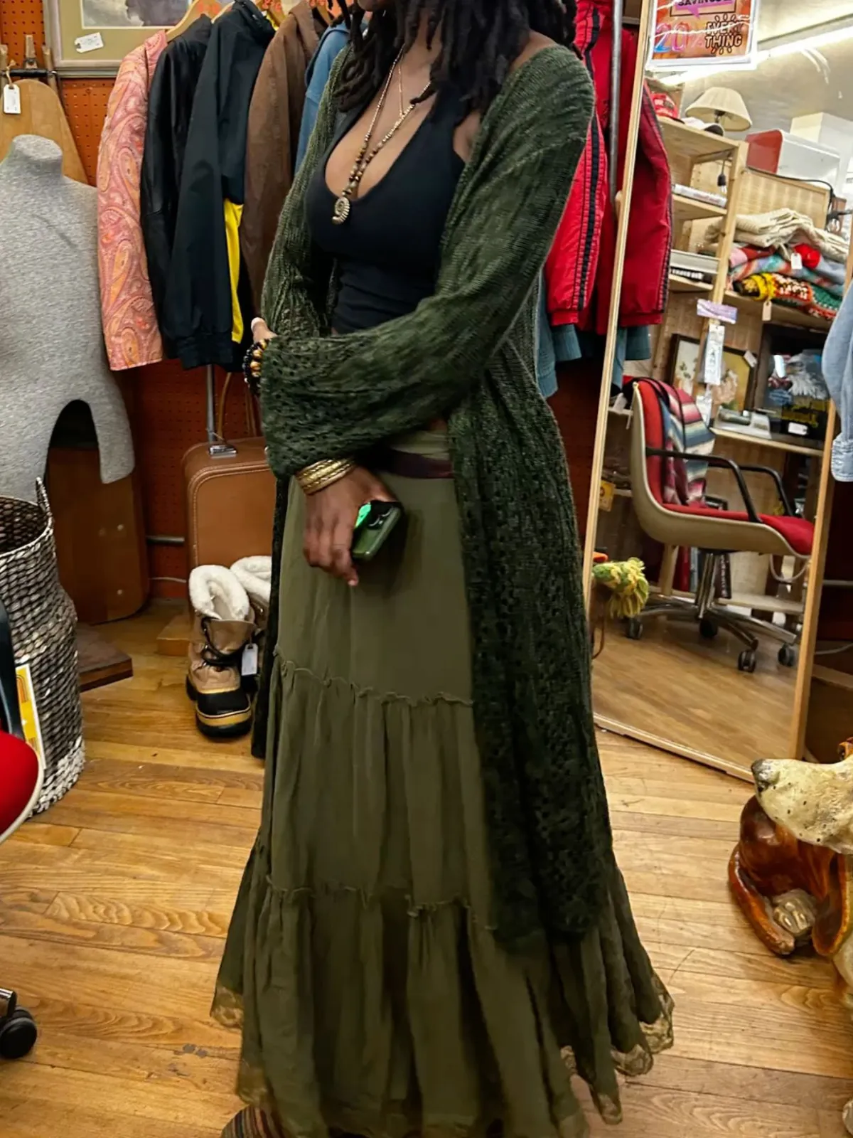 Earthy Black Girl aesthetic — The long, tiered olive skirt, knit cardigan, natural hair, and stacked jewelry are all strong indicators of the Earthy Black Girl aesthetic, particularly the emphasis on natural fabrics and relaxed silhouettes.