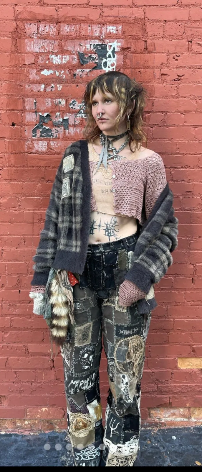 Gutter Punk aesthetic — The heavily patched and layered clothing, distressed knitwear, hand-poked tattoo aesthetic, and overall 'apocalypse-grime' look strongly align with the description's visual signature and palette.