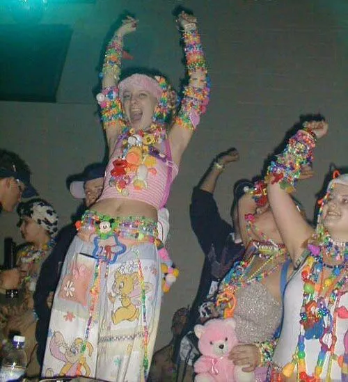 Kandi Raver aesthetic — The image perfectly captures the early 90s rave scene with stacked kandi bracelets, fluffy accessories, and children's show iconography on the pants.