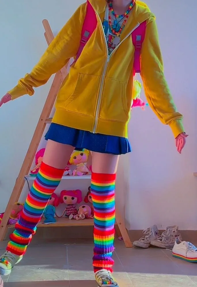 Kidcore aesthetic — Rainbow striped leg warmers, bright primary colours, and a backpack evoke the playful, nostalgic imagery of 90s/early-2000s childhood.