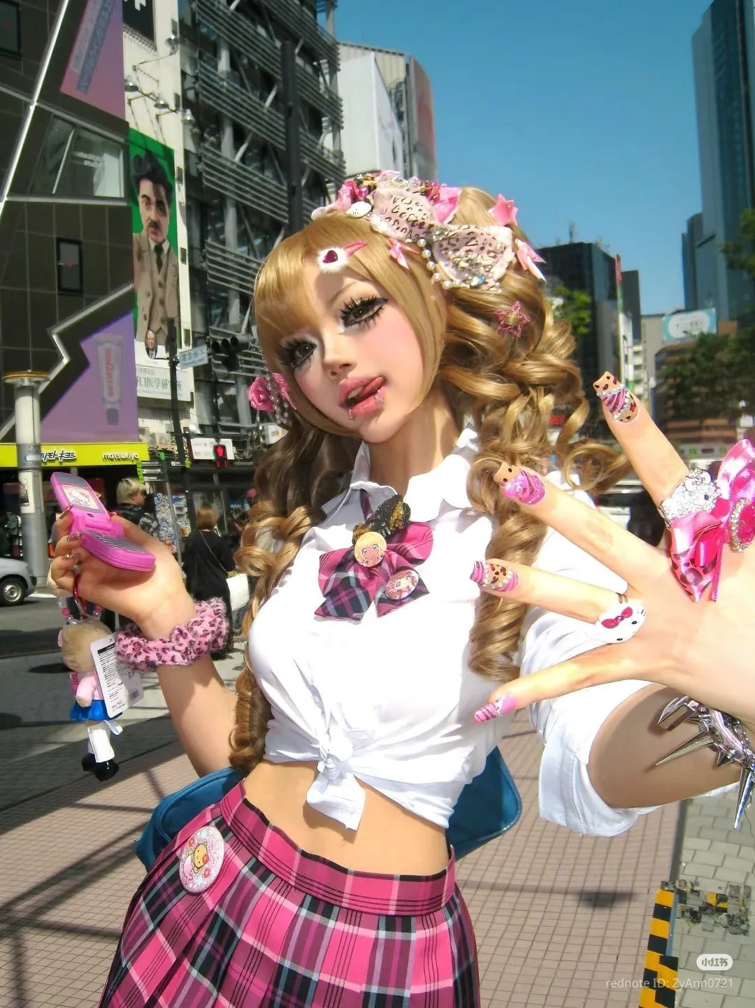 Kogal aesthetic — The ultra-short plaid skirt, tied-up sailor-style shirt, bleached blonde hair, heavy makeup, and abundance of accessories (including a Burberry-check inspired bow) perfectly capture the Kogal aesthetic.