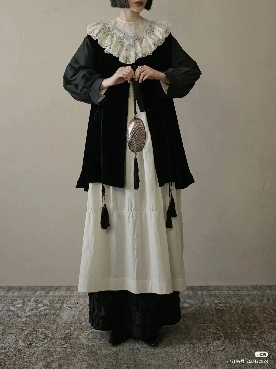 New England Gothic aesthetic — The high ruffled lace collar, dark velvet capelet over a white dress, and antique-style silver accessory directly evoke the Puritan and folk-gothic elements described, especially the white linen collars and mourning jewellery.