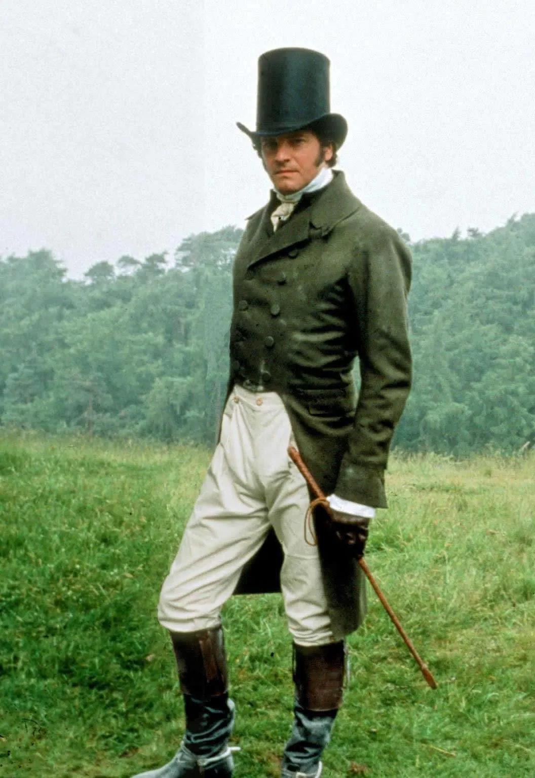 Regency aesthetic — Colin Firth as Mr. Darcy in a green tail-coat, white breeches, top hat, and boots, is an iconic representation of Regency menswear, matching the description's visual signature.