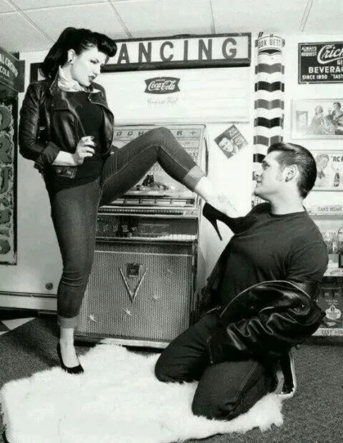 Rockabilly aesthetic — The woman's leather jacket, cuffed jeans, cat-eye liner, and hairstyle, along with the man's greaser look and the diner setting, are perfect Rockabilly references.