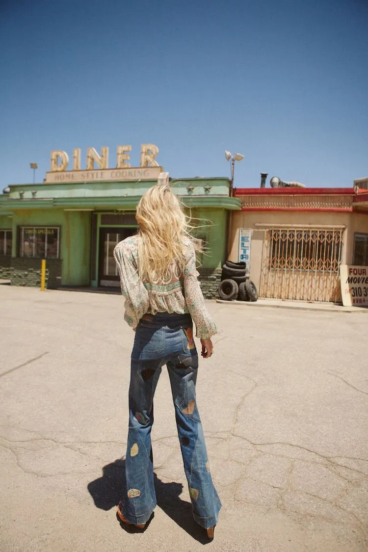 Route 66 aesthetic — The diner setting, flared patched jeans, and overall styling are a perfect encapsulation of the mid-century Route 66 aesthetic.