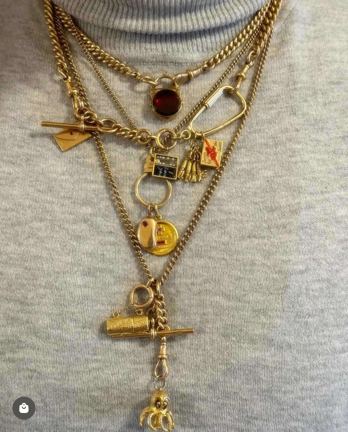 Trinketcore aesthetic — Dense layering of gold chains with diverse, small historical-looking charms (envelope, quill, seal, skull, eye) is a perfect visual representation of the aesthetic's core concept.