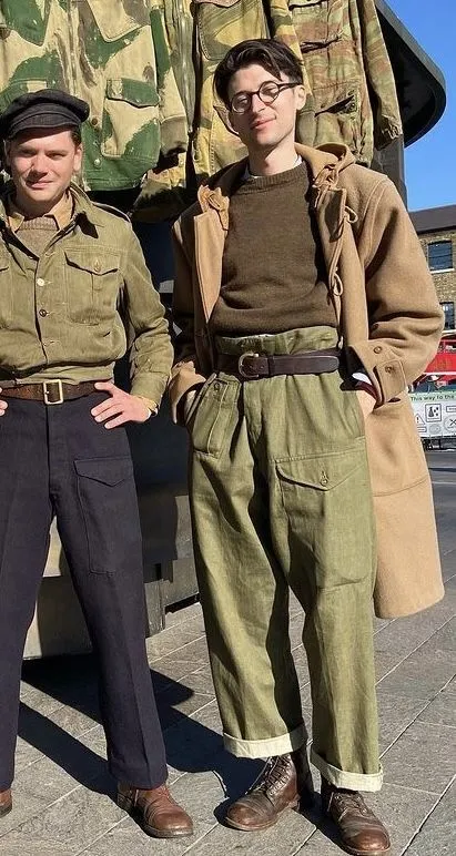 Wartime Austerity aesthetic — The khaki jacket, olive green high-waisted trousers with patch pockets, and the overall muted palette strongly represent the L-85 regulations and wartime utility clothing.