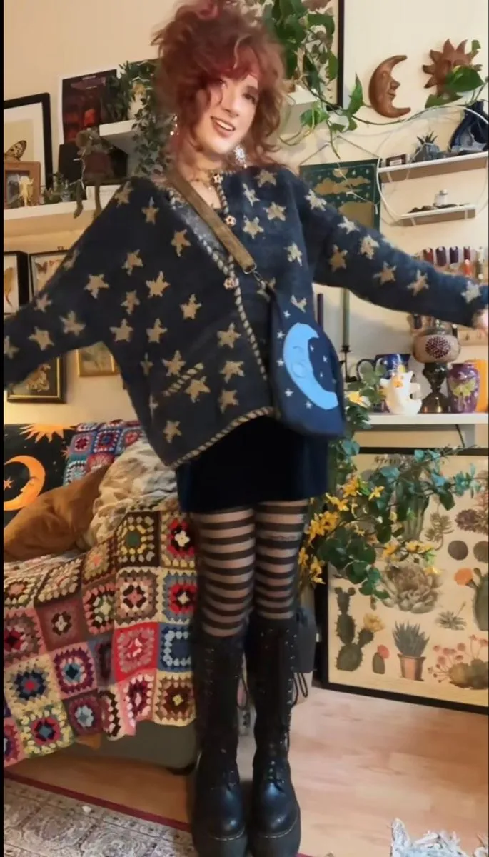 Whimsigoth aesthetic — The outfit strongly aligns with the Whimsigoth aesthetic, featuring celestial motifs (stars on the cardigan, moon on the bag), layered jewelry, a velvet dress, and chunky platform boots. The overall vibe is mystical and witchy, fitting the description perfectly.