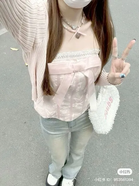 Wonyoungism aesthetic — The pink corset top with a large bow, lace trim, and the soft pink cardigan strongly evoke the ballerina-coquette and high-feminine aspects. The pearl necklace and the fluffy heart bag are also fitting accessories.